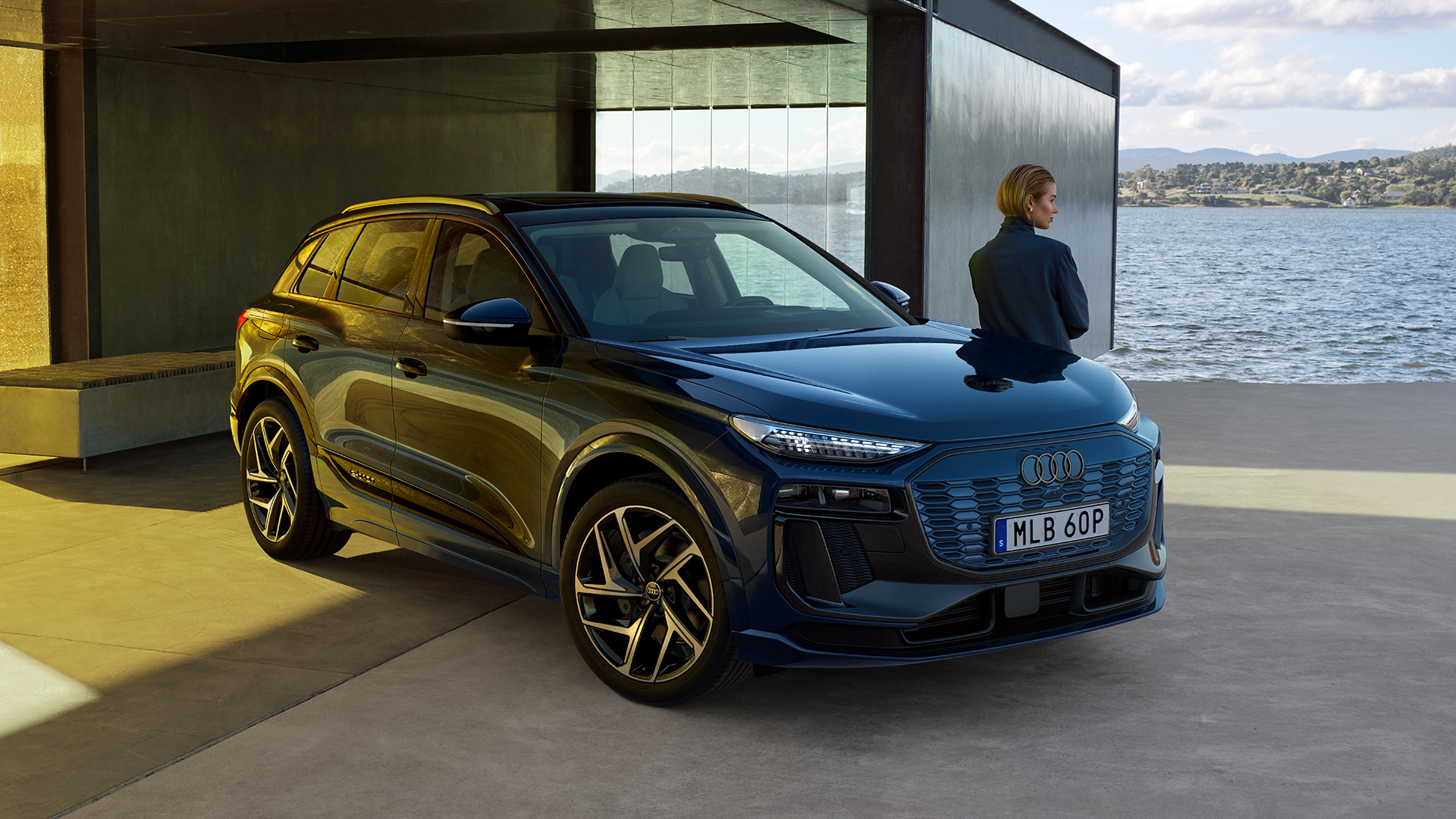 Kvvinna står och lutar sig mot sin Audi A6 e-tron samt blickar bort mot landskapet