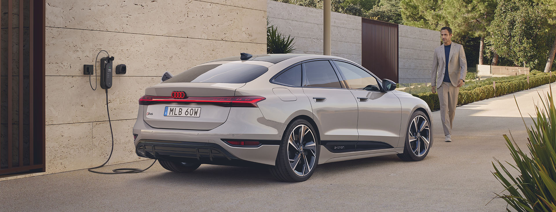 Audi A6 Sportback e-tron står parkerad framför ett stenhus, man närmar sig bilen för att åka ivär