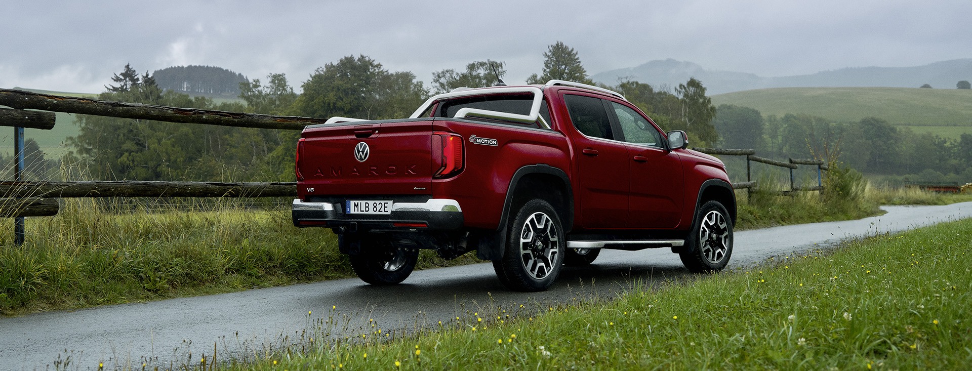 Röd Amarok Style, sedd snett bakifrån då den kör på landsväg i grönskande landskap