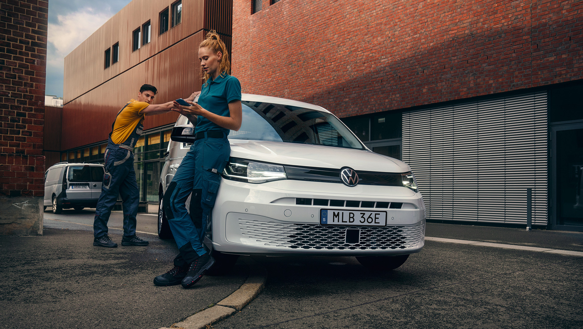 En kille och tje i arbetskläder står vid en VW Caddy Proline på en smal gata mellan tegelhus