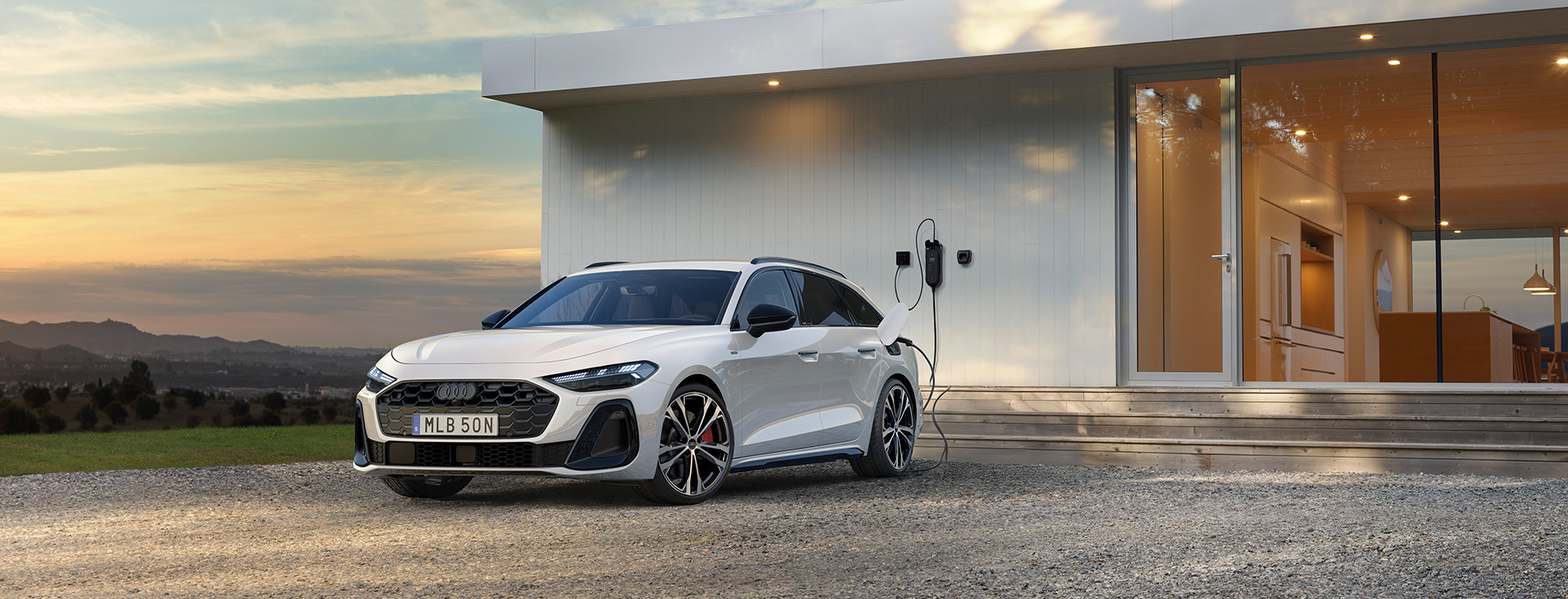 Audi A5 Avant e-hybrid står parkerad framför vitt putshus med laddaren ikopplad