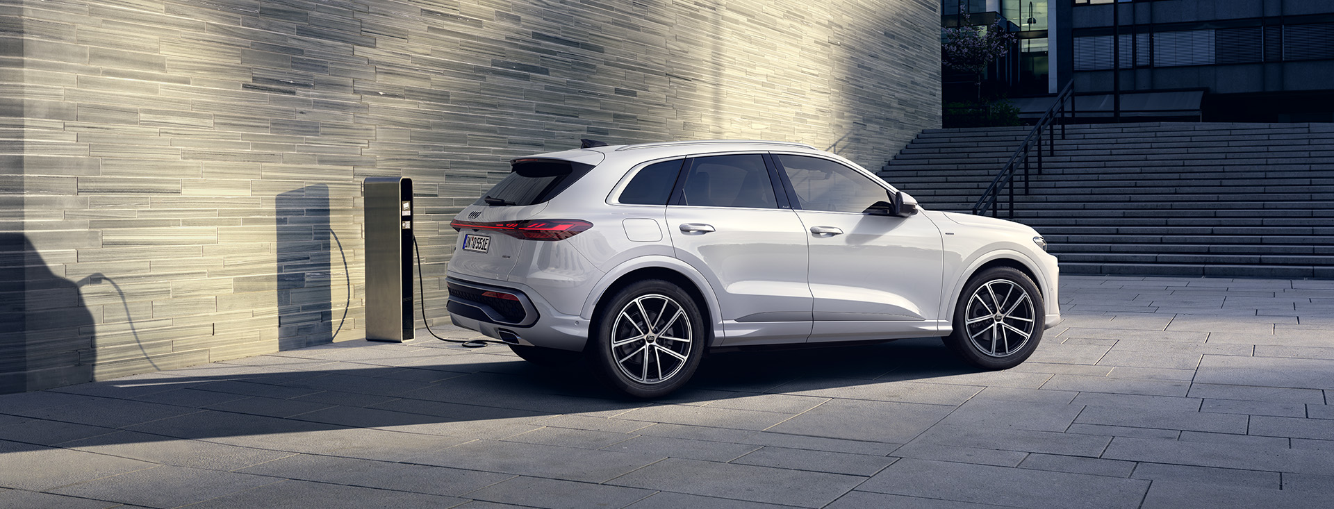 En vit Q5 e-hybrid quattro parkerad vid tegel-höghus med laddsladd i